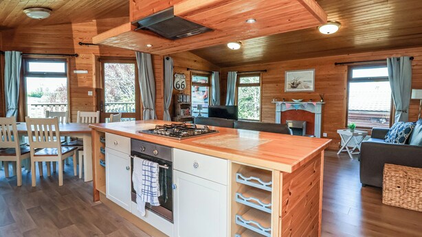 A cozy cabin-style room with a wooden interior, a central island with a stove, a dining area, and a fireplace. - The Beach House (Ilfracombe)