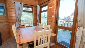 A wooden cabin with a dining table and chairs, large windows, and a deck. - The Beach House (Ilfracombe)