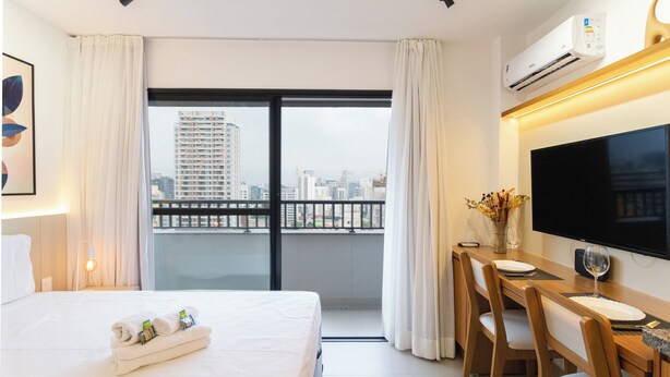 Ein Hotelzimmer mit Bett, Schreibtisch mit Stuhl, Flachbildfernseher und Balkon mit Stadtblick.