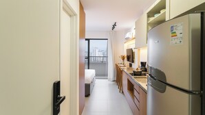 Eine schmale Hotelküche mit Kühlschrank, Kaffeemaschine und Fenster mit Blick auf eine Stadtlandschaft.