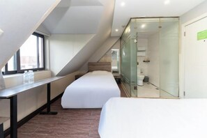 A modern hotel room with a lofted sleeping area, a glass partition, and a view of the city.