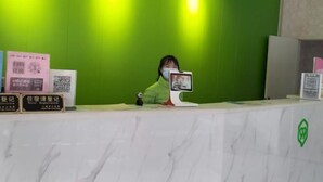 A reception desk with a green wall and a marble counter. There are signs for hotel registration and a QR code.