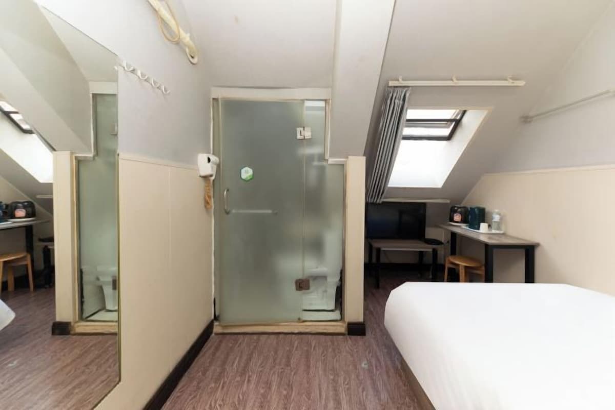 Una camera d'albergo con un letto, una scrivania, una sedia, un tavolino e una porta in vetro che dà sul bagno.