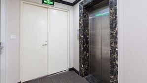 An elevator with a marble wall, a white door with an exit sign, and a grey floor.