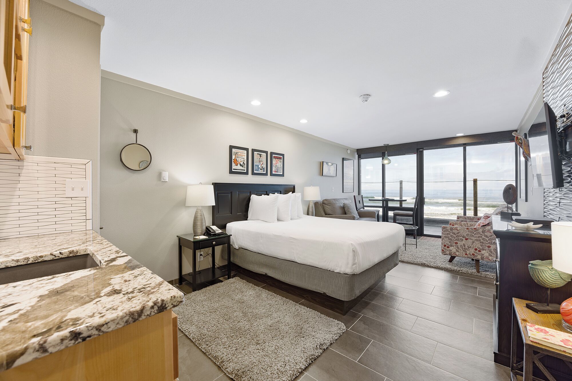 Habitación de hotel con cama, escritorio, silla, ventana grande con vistas y baño con espejo e inodoro.