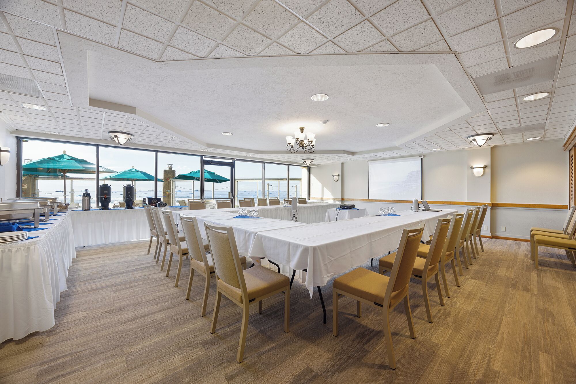 A conference room with a long table, chairs, and a view of the sea through large windows.