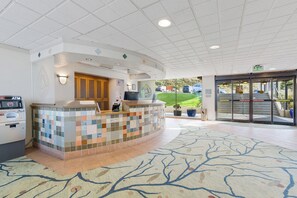 A hotel lobby with a reception desk, an ATM, and a view of the parking area.