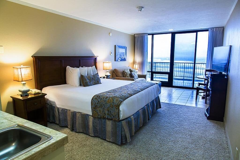 Ein Hotelzimmer mit einem großen Bett, einem Schreibtisch, einem Sessel, einem Fernseher und einem Balkon mit Aussicht.