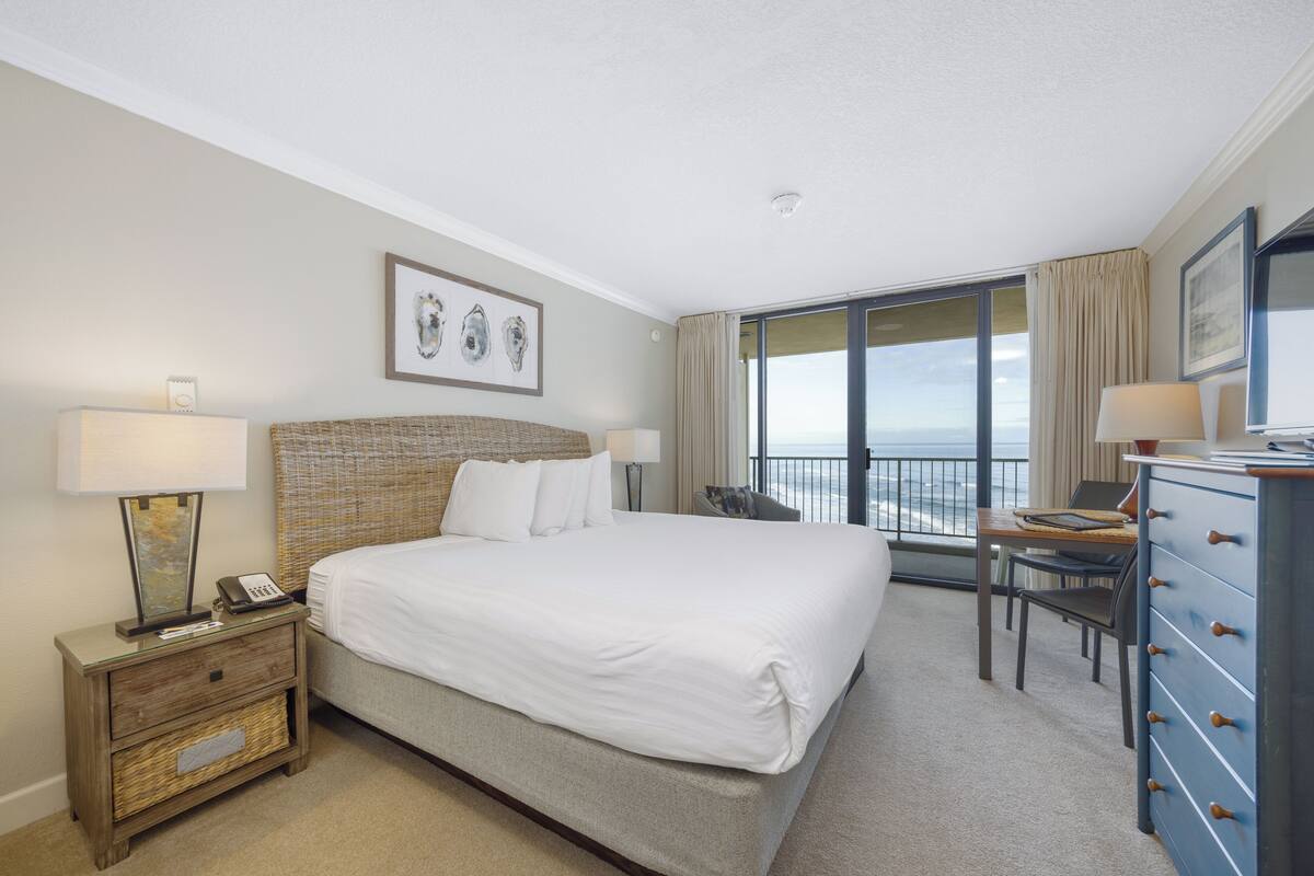 Un cuarto de hotel con una cama grande, un escritorio, un aparador y vista al océano.
