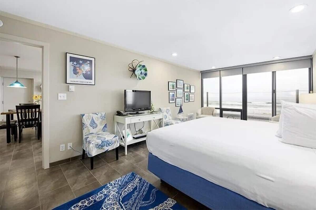 Habitación de hotel con una cama grande, un escritorio con computadora, una silla y vista al océano.