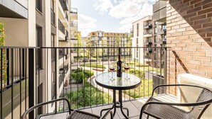 A balcony with a table and chairs, overlooking a courtyard with buildings and greenery.