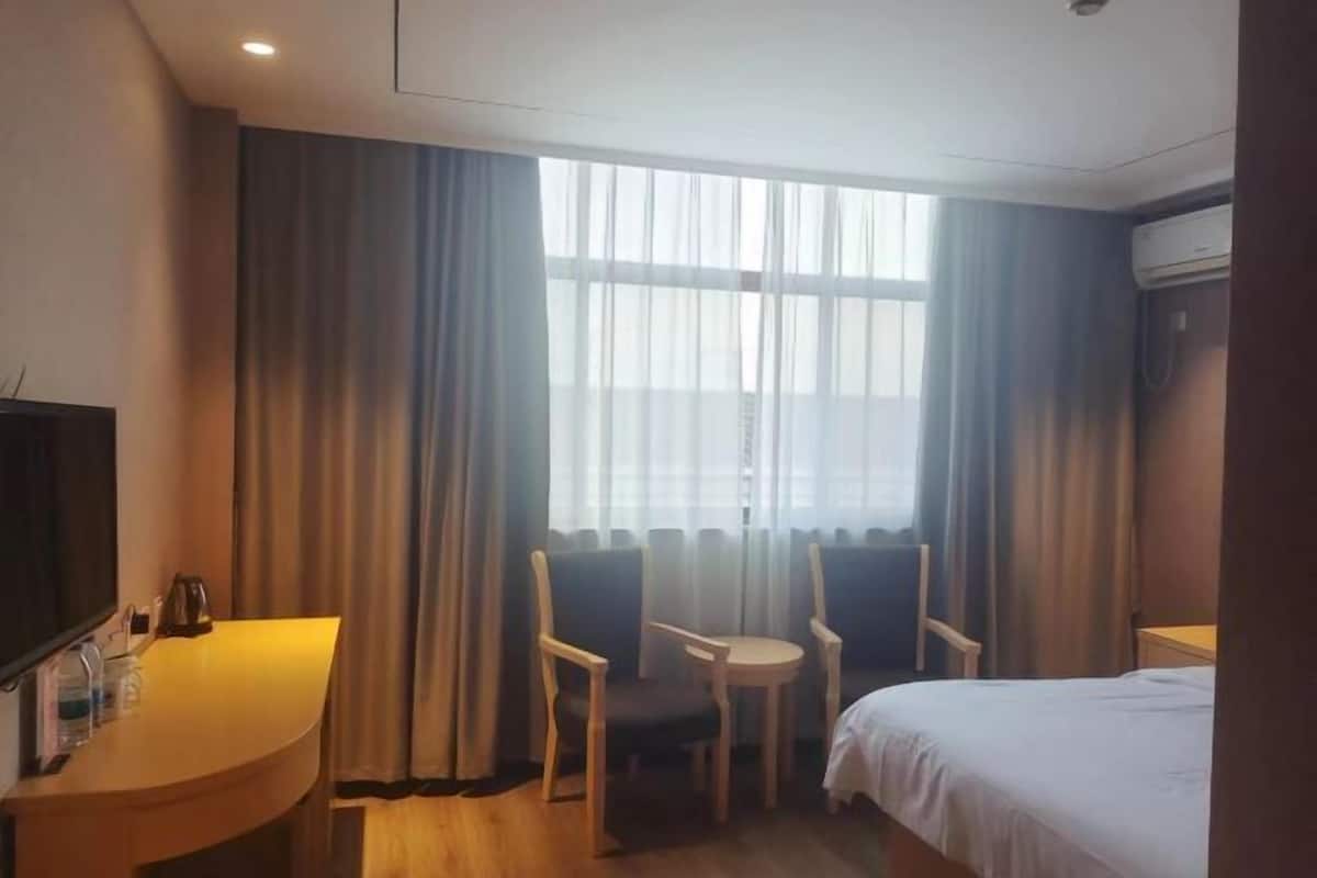 Una camera d'albergo con un letto, una scrivania con una sedia, un tavolino con due sedie e un'ampia finestra con tende.