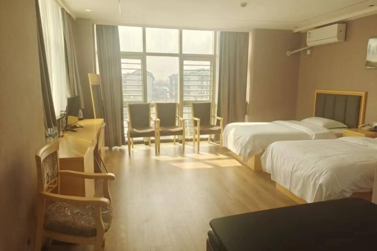 Camera d'albergo con una grande finestra, due letti, una scrivania con una sedia e un tavolino.