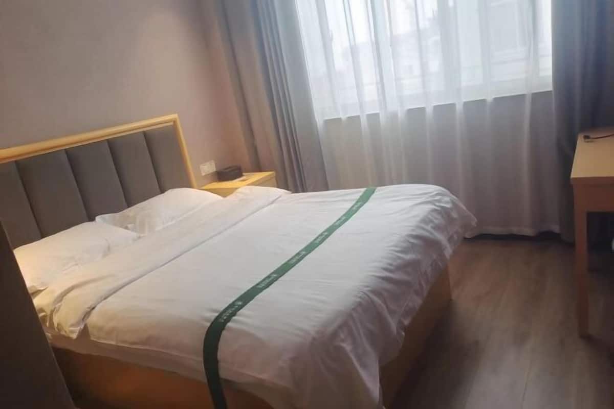 Una camera d'albergo con un letto, un comodino, una scrivania e una finestra con tende.