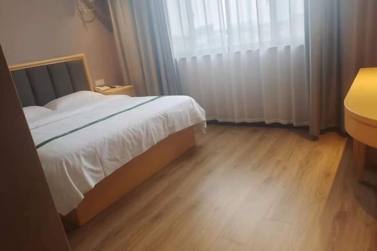 Una camera d'albergo con un letto, un comodino, una lampada e una finestra con tende.