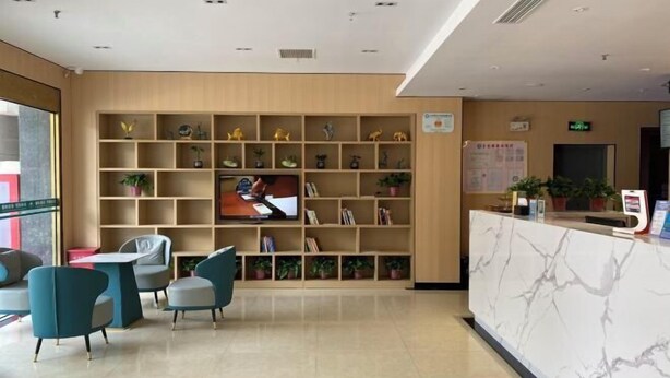 Un hall d’hôtel comprenant un comptoir d’accueil, un espace salon et un mur recouvert d’étagères où sont disposées des plantes en pot.