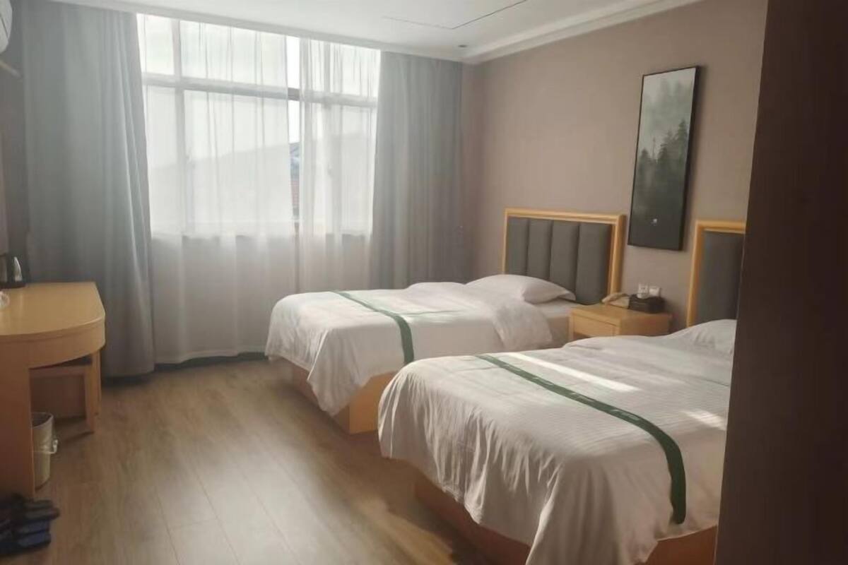 Camera d'albergo con due letti, una scrivania, una sedia, una finestra con tende e un quadro appeso al muro.