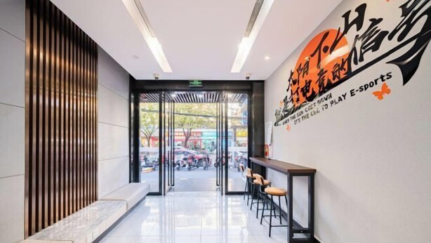 A modern interior with a reception area, a seating area with stools, and a wall with a logo. - Jiting E-sports Hotel (Wujiaochang Shanghai Sports University Branch) (Shanghai)