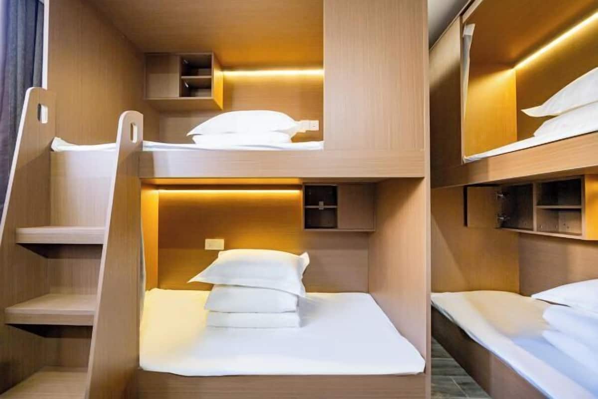 A bunk bed room with wooden walls, a small shelf, and a bedside table.