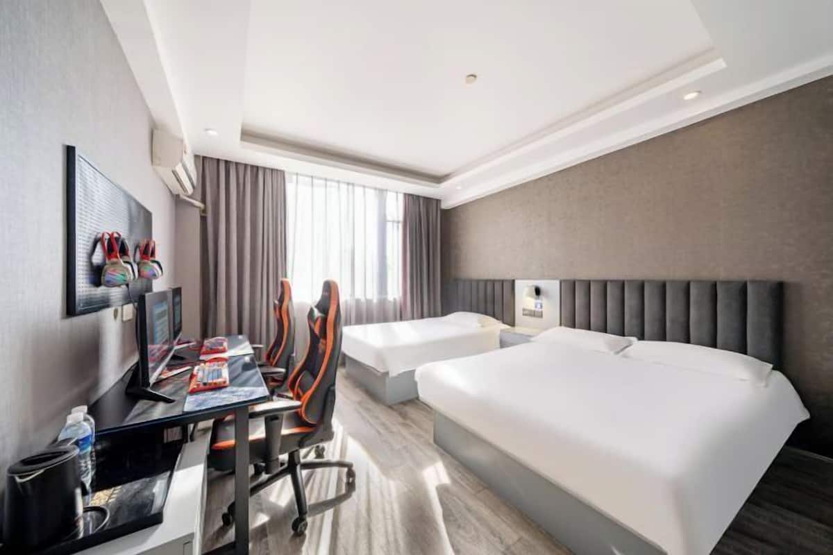 A hotel room with a desk, two gaming chairs, a bed, and a large window with curtains.