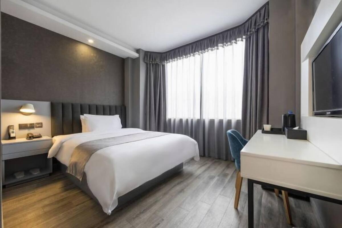 A modern hotel room with a large bed, a desk, and a TV.