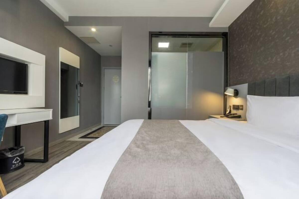 A modern hotel room with a bed, bedside table, lamp, and a mirror.