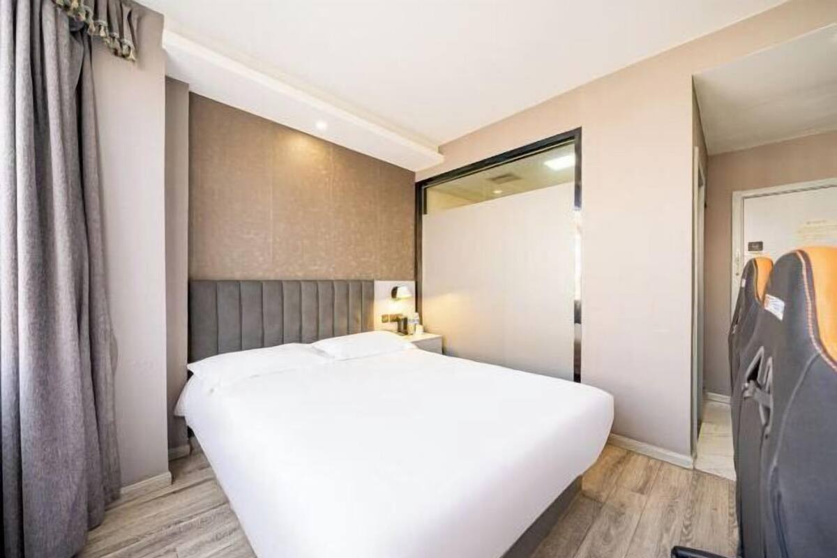 A hotel room with a bed, a nightstand, a lamp, a mirror, and a wardrobe.