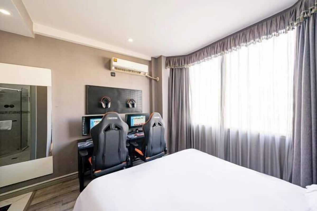 A hotel room with a bed, a desk with two chairs, a glass shower enclosure, and a large window with curtains.