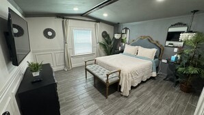 Une chambre à coucher comprenant un lit, un banc, une commode, un miroir et un téléviseur.