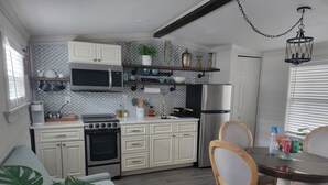 Une cuisine moderne avec des meubles blancs, un four à micro-ondes encastré, un réfrigérateur en acier inoxydable et un coin repas comprenant une table et des chaises en bois.