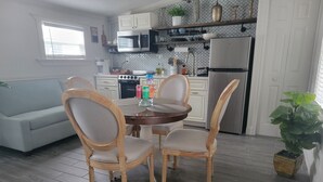 Une cuisine moderne avec des meubles blancs, un réfrigérateur en acier inoxydable et un coin repas comprenant une table ronde en bois et quatre chaises.