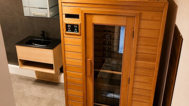 A sauna with a wooden exterior, a control panel, and a glass door.