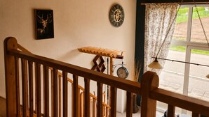 A wooden staircase with a railing, a wall clock, a framed picture, and a window with curtains.