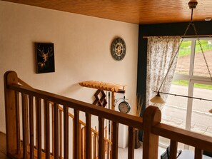A wooden staircase with a railing, a wall clock, a framed picture, and a window with curtains.