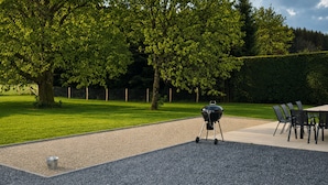 A patio area with a barbecue grill, outdoor seating, and a hedge.