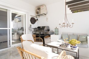 A modern living room with a sliding glass door, a grill, a chandelier, and a sofa with cushions. - Mairena 23 - Sea view apartment (Ojen)