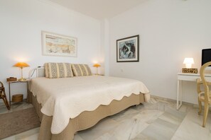 A bedroom with a bed, two bedside tables with lamps, a desk, and two chairs.