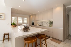 A modern kitchen with a marble countertop, wooden stools, and a large island. - Mairena 23 - Sea view apartment (Ojen)