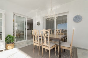 A dining area with a wooden table and chairs, a chandelier, and a view through a glass door. - Mairena 23 - Sea view apartment (Ojen)