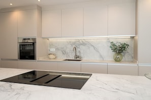 A modern kitchen with a built-in oven, a stainless steel sink, and a marble backsplash. - Mairena 23 - Sea view apartment (Ojen)
