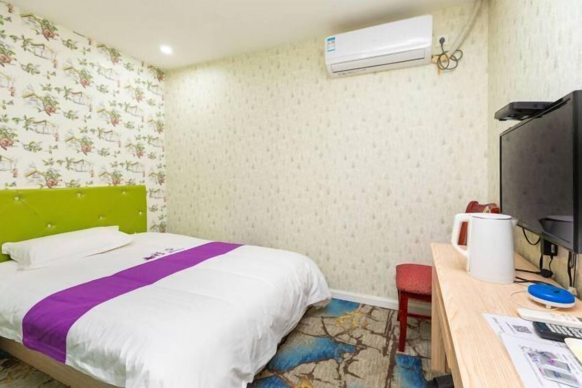Ein Hotelzimmer mit einem Bett, einem Schreibtisch mit Computer, einem Sessel, einer Klimaanlage und einem Fernseher.