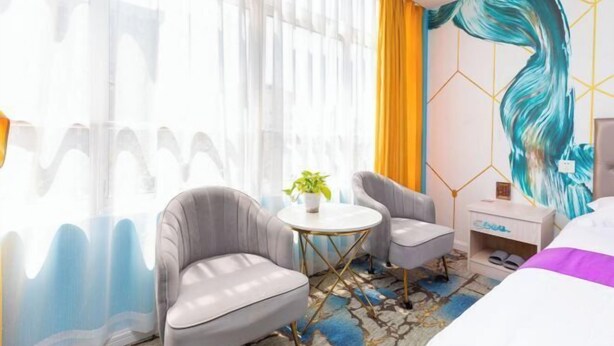 Habitación de hotel con una cama, dos sillones, una mesita, una planta y un cuadro abstracto grande en la pared.