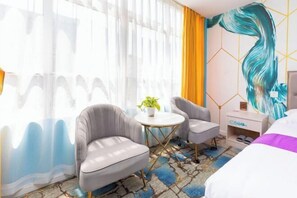 A hotel room with a bed, two armchairs, a small table, a plant, and a wall with a large abstract painting. - Colorful Art Hotel Shanghai (Shanghai)