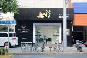 Entrada de un hotel con fachada negra, un cartel y una bicicleta estacionada afuera.