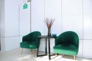 A room with two green upholstered chairs, a small round table, and a vase with branches. - Colorful Art Hotel Shanghai (Shanghai)