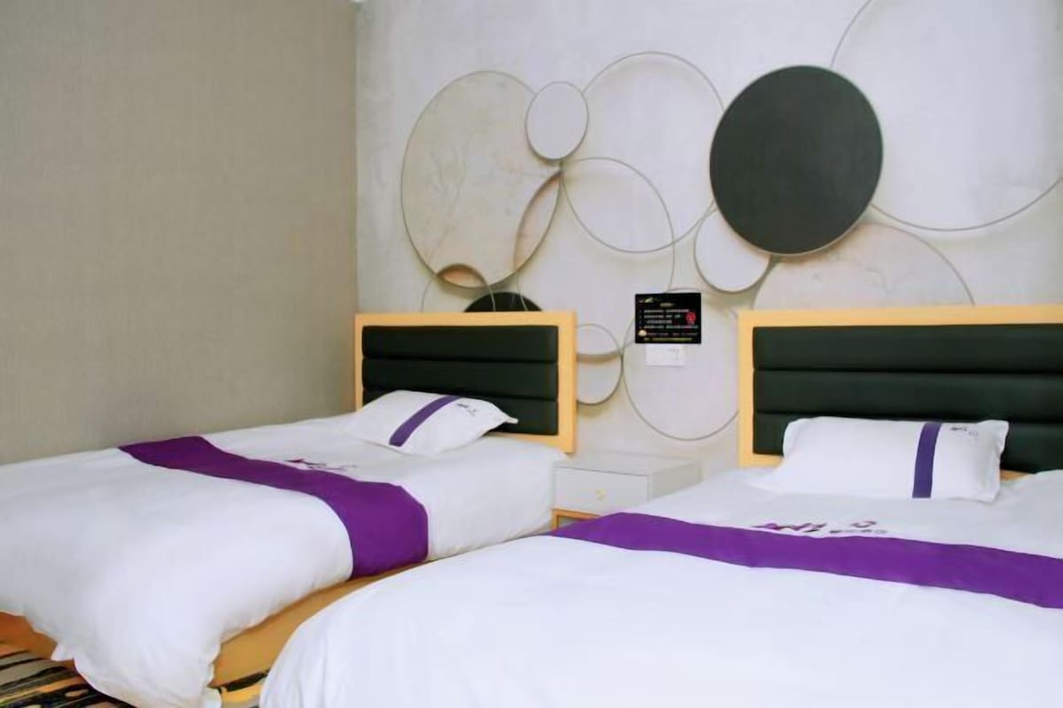 A hotel room with two beds, a modern wall design, and a small bedside table.