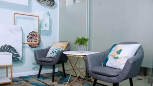 Una habitación con dos sillones grises, una mesa redonda pequeña, una mesita auxiliar blanca y una pared con arte abstracto.