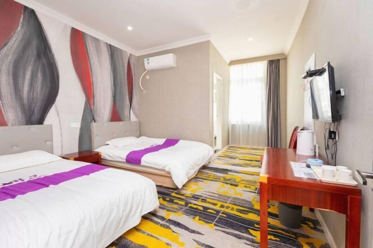 Ein Hotelzimmer mit zwei Betten, einem Schreibtisch, einem Fernseher und einer Klimaanlage.