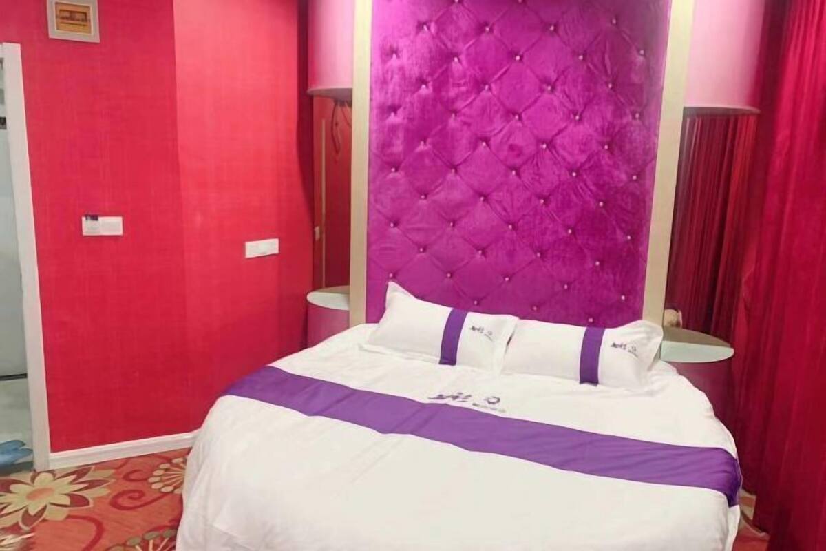 Ein Hotelzimmer mit einem großen Bett, einem gepolsterten Kopfteil und roten Wänden.