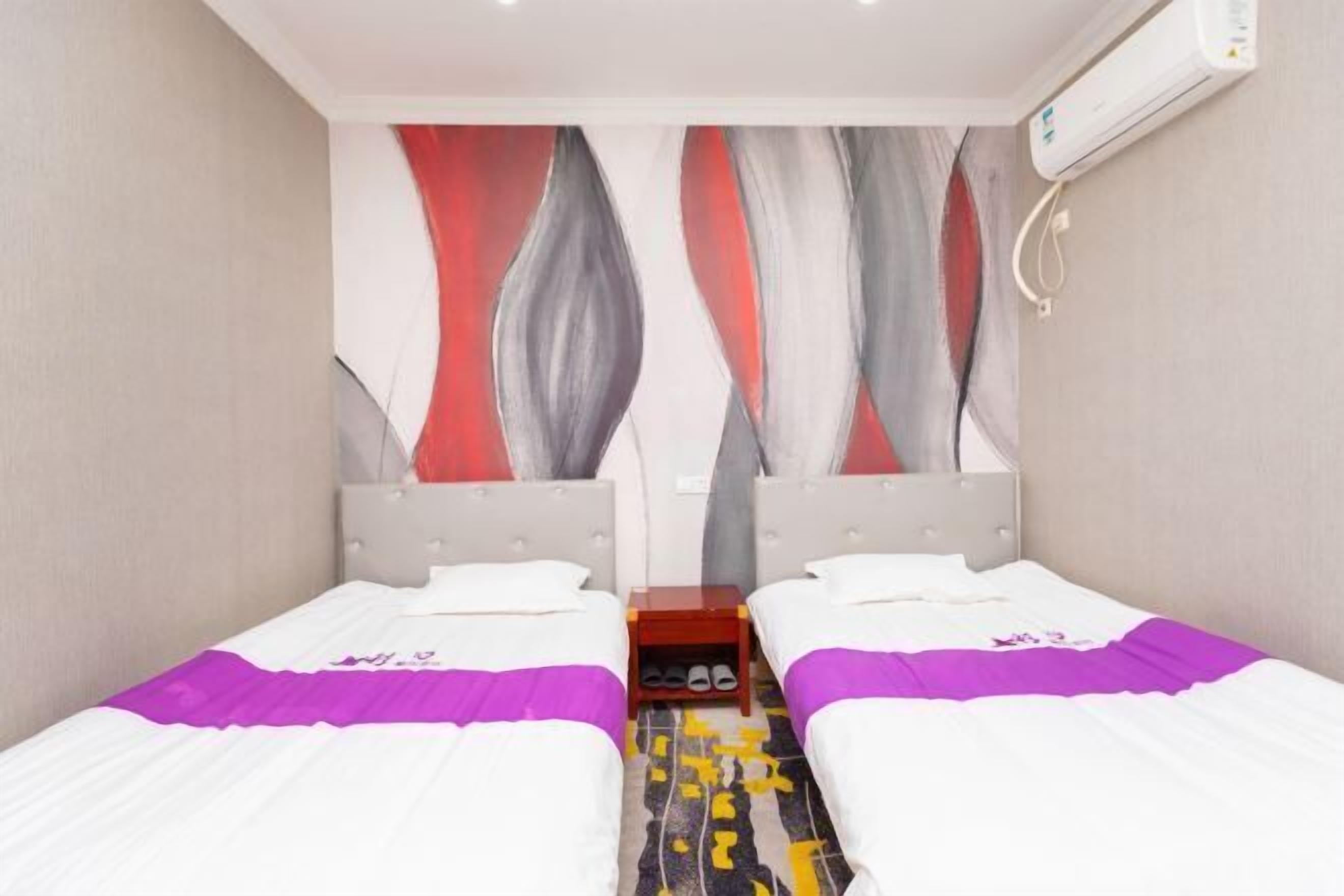 Una habitación de hotel con dos camas, una mesita pequeña y un aire acondicionado instalado en la pared.